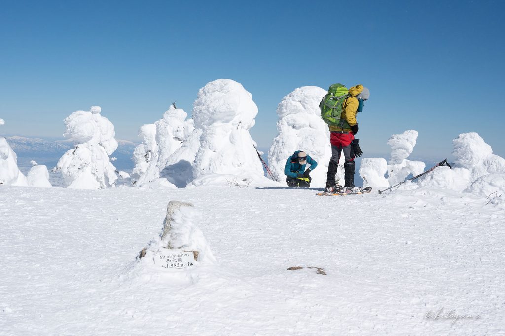 西大巓の山頂標識と休憩する登山者