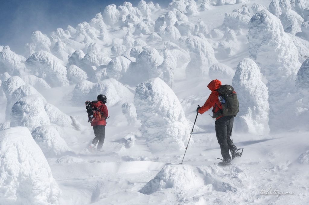 雪に完全に覆われた樹氷の周りを歩く登山者たち