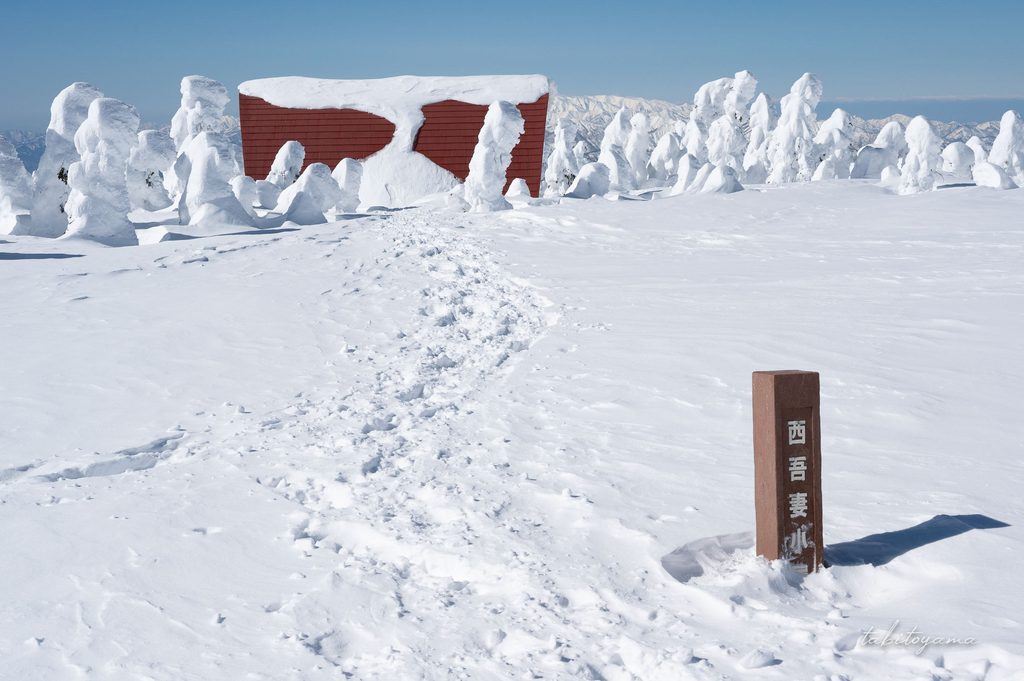 雪に埋もれた西吾妻避難小屋の立て看板と小屋へと続くトレース