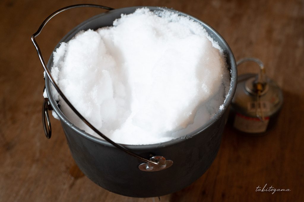 クッカーいっぱいに詰められた雪をバーナーで溶かす様子