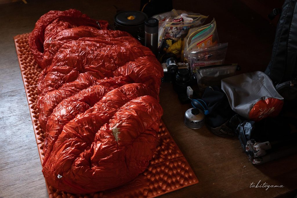 避難小屋の中に広げられた荷物と寝袋、マット