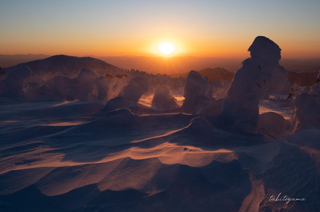 夕日を受けて陰影が強くついた雪原とシルエットになる樹氷