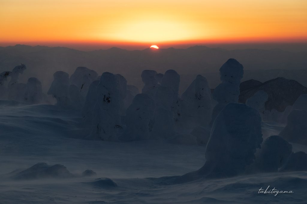 日没寸前の太陽と暗い雪原に立つ樹氷たち