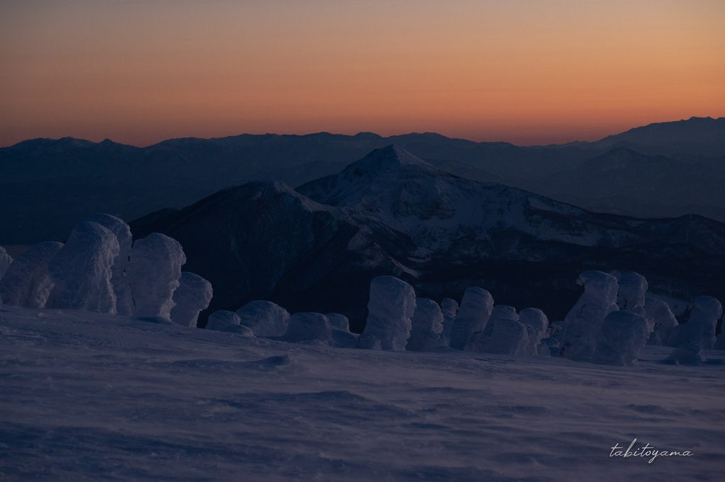 オレンジ色の帯状に染まる夕焼けの空と磐梯山と樹氷原