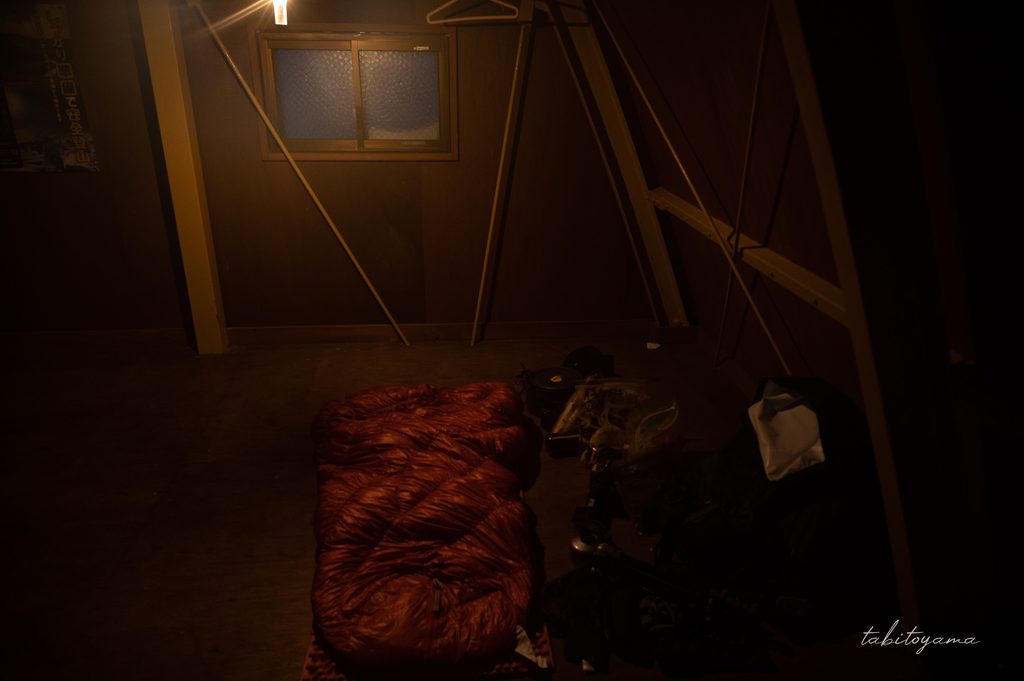 避難小屋の中に吊るしたランタンの微かな灯りに照らされる寝袋や荷物