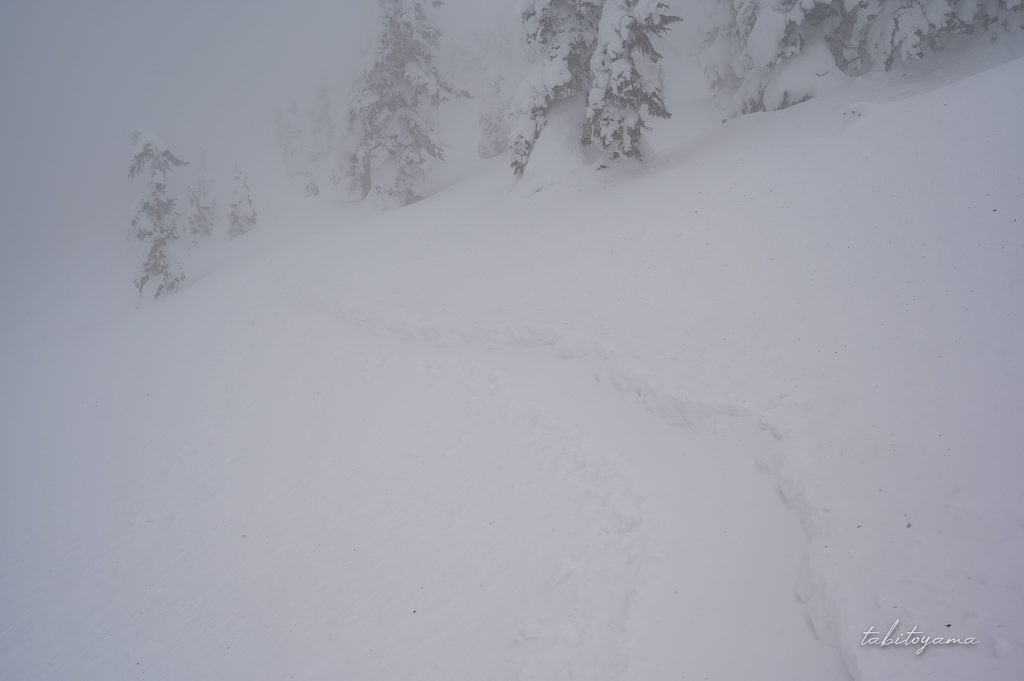 吹雪で視界が悪化するなか、わずかなトレースを頼りに進む登山道
