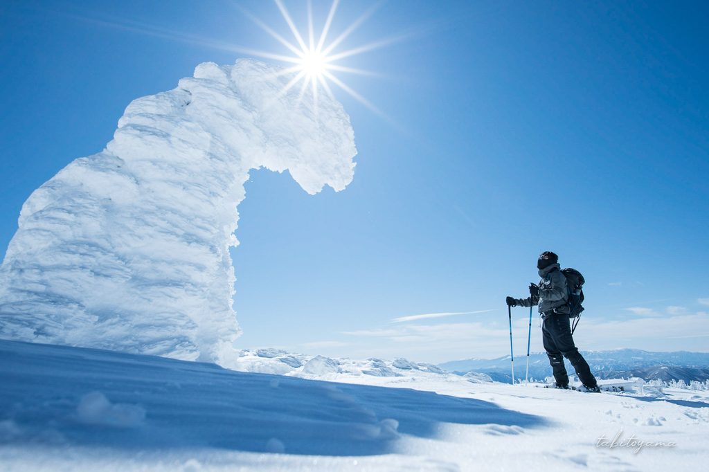 太陽の光芒の下で大きな樹氷と向き合う登山者