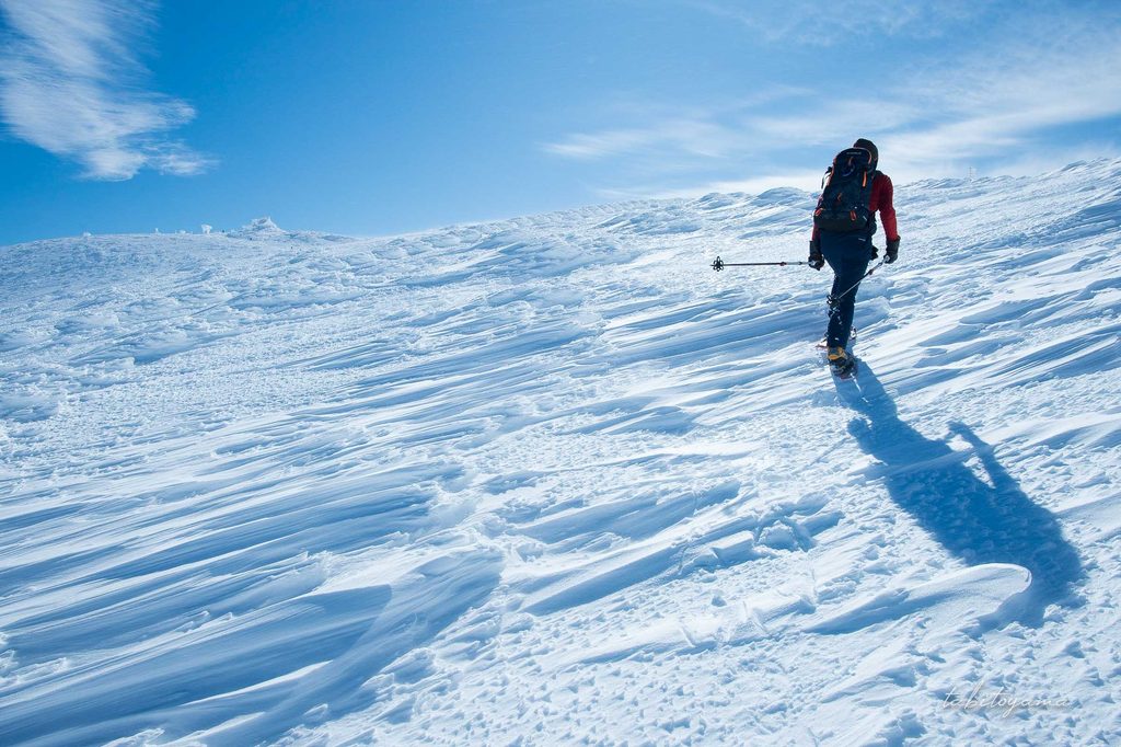 シュカブラが刻まれた雪の斜面を歩く登山者の姿