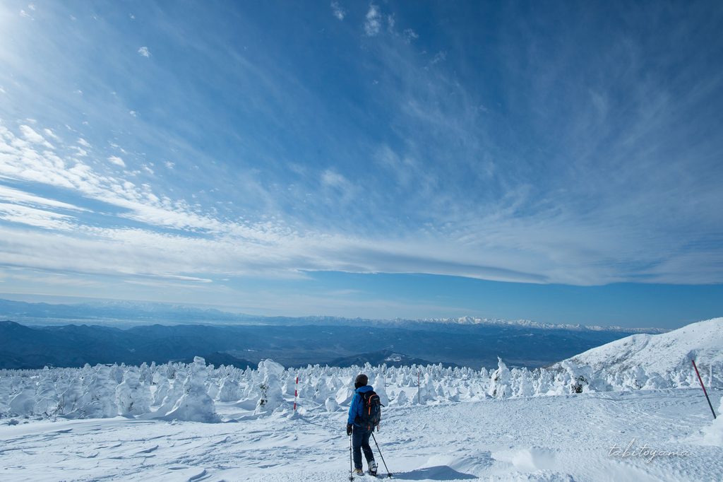 飯豊連峰と朝日連峰を蔵王の樹氷原から見渡す登山者の姿