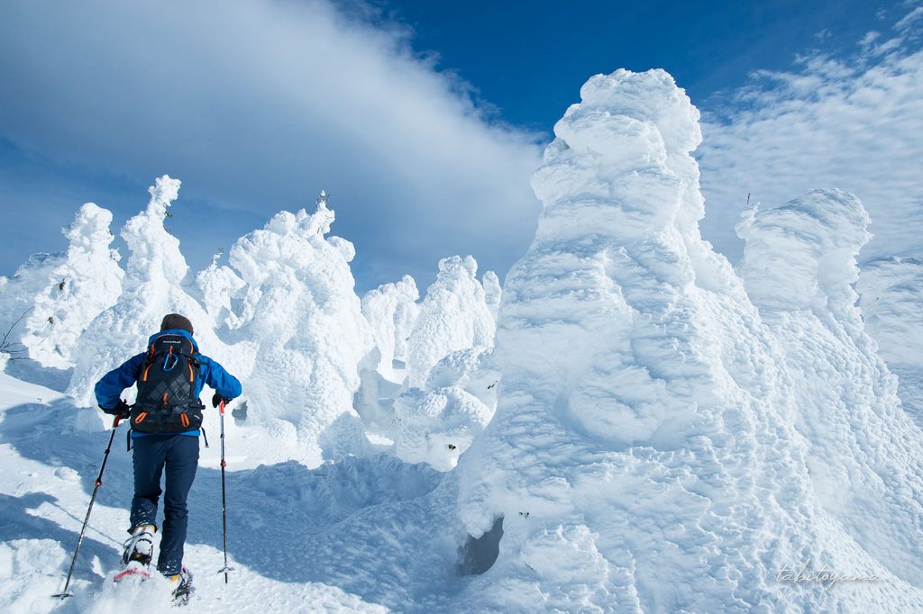 大きな樹氷の脇を雪を蹴り上げながら登る登山者の姿