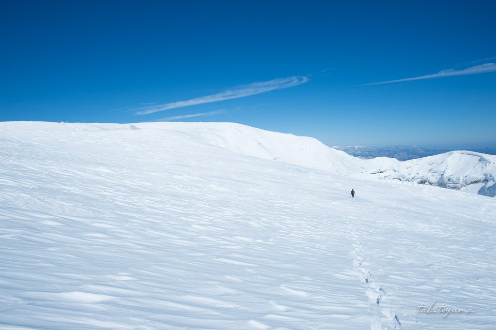 雪の蔵王山の広大な稜線を歩く小さな登山者の姿